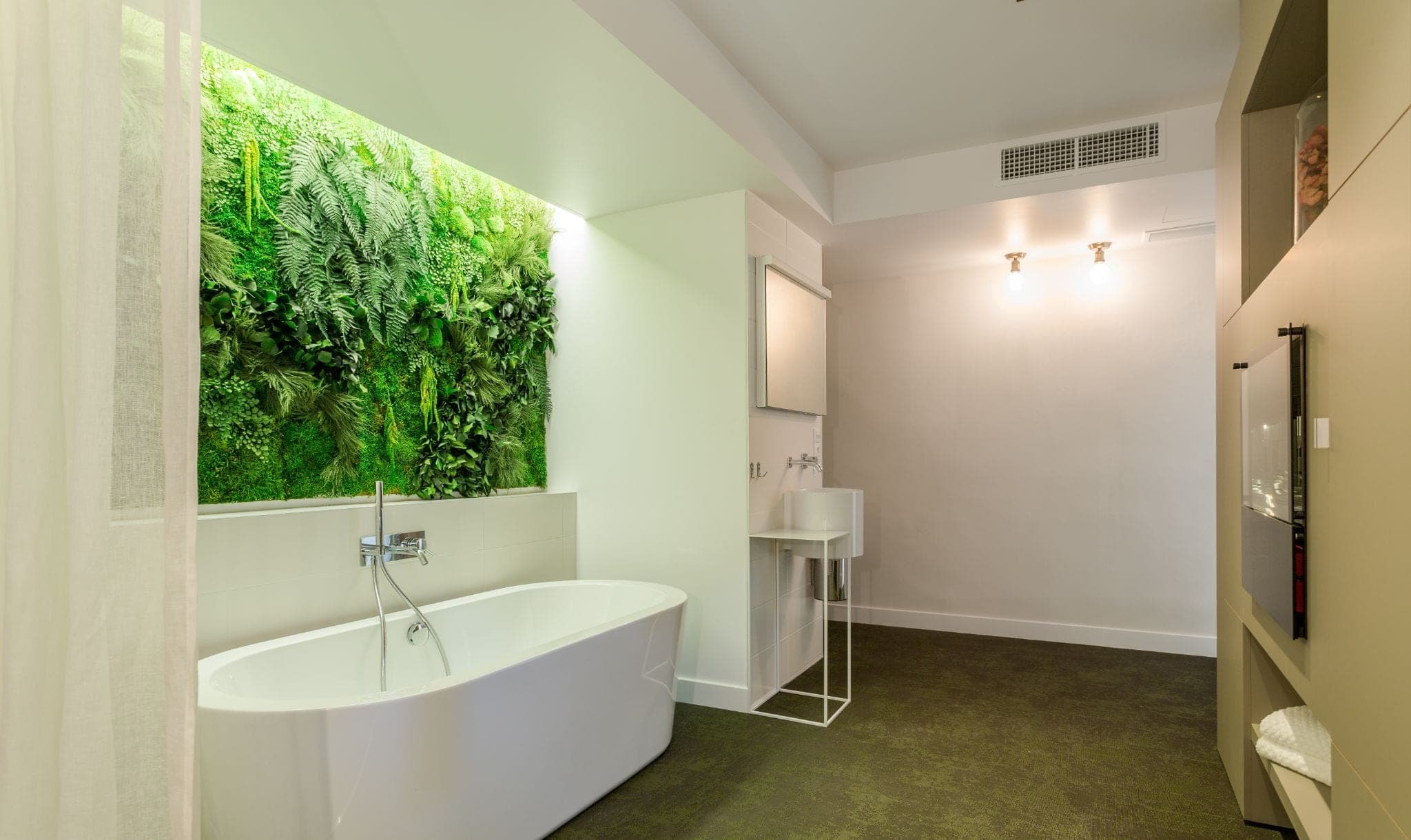 Baignoire îlot devant un mur végétal, sol vert et murs blancs