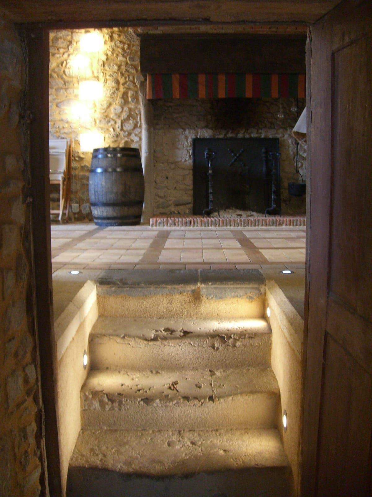 Escalier en pierre éclairé menant à une cave voûtée avec cheminée