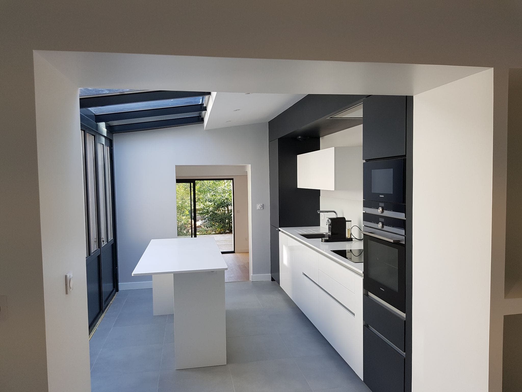 Cuisine blanche et anthracite sous verrière de toit, avec îlot central