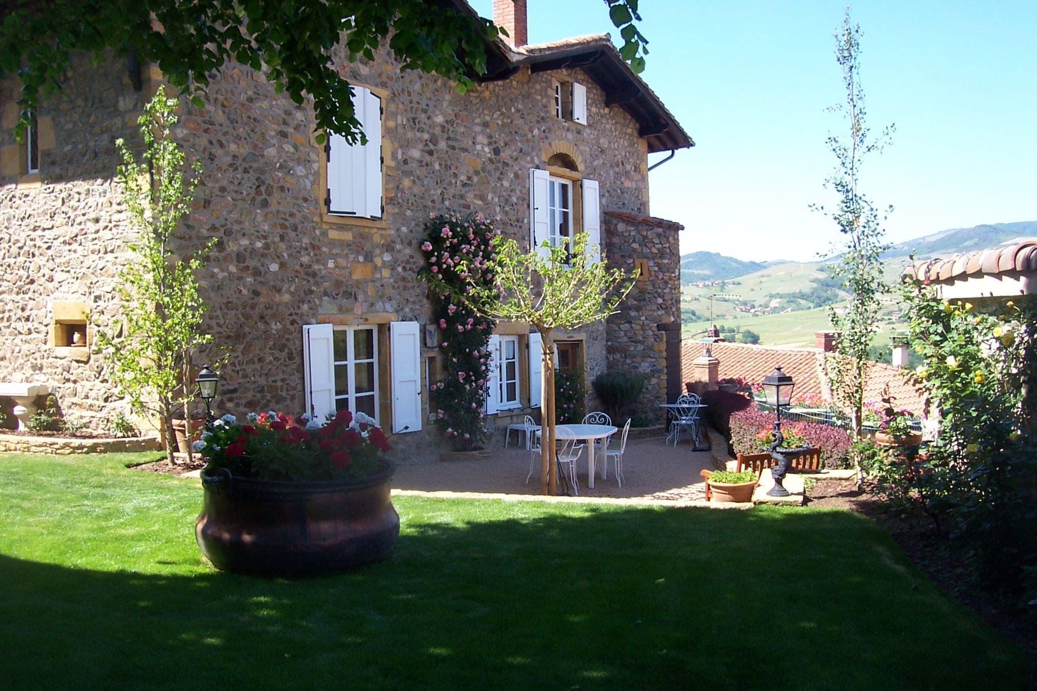 Maison en pierre rénovée avec volets blancs et jardin