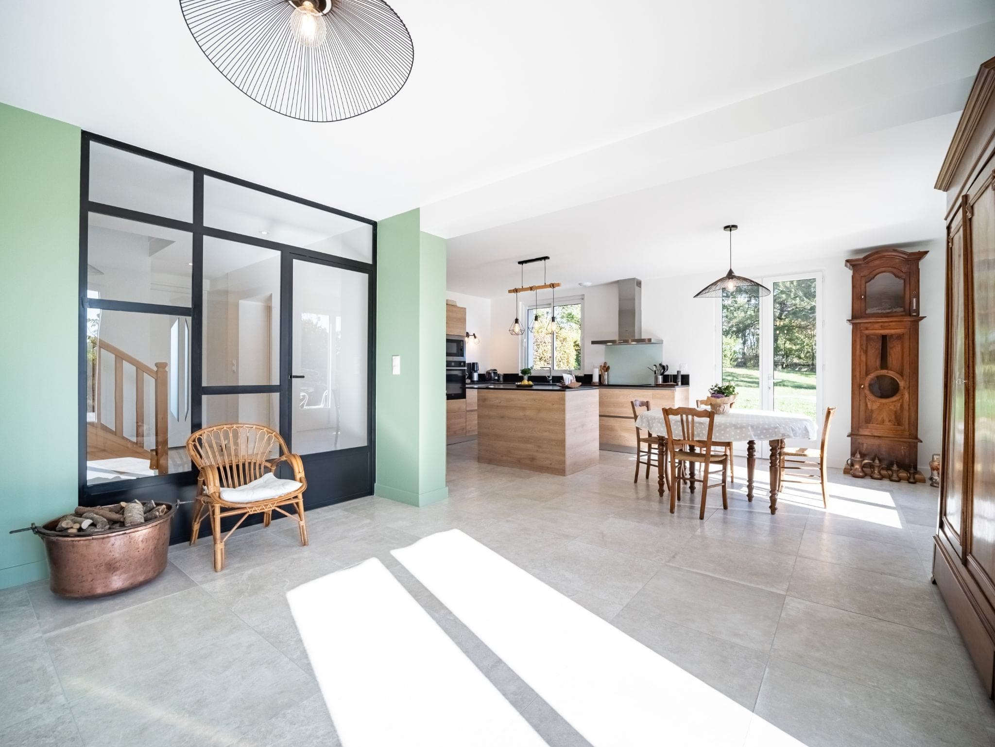 Pièce de vie ouverte avec verrière d’atelier noire, mur vert d’eau et cuisine en fond