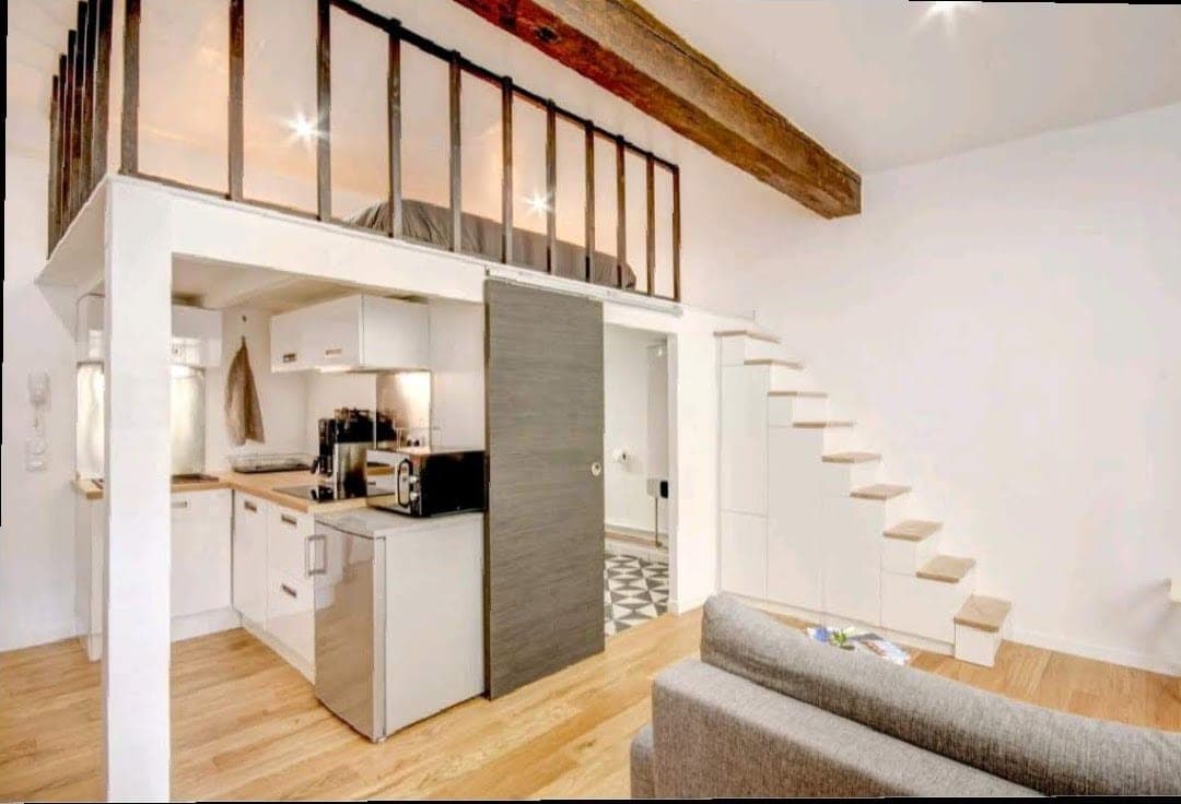 Studio avec cuisine sous mezzanine, escalier blanc et poutre apparente