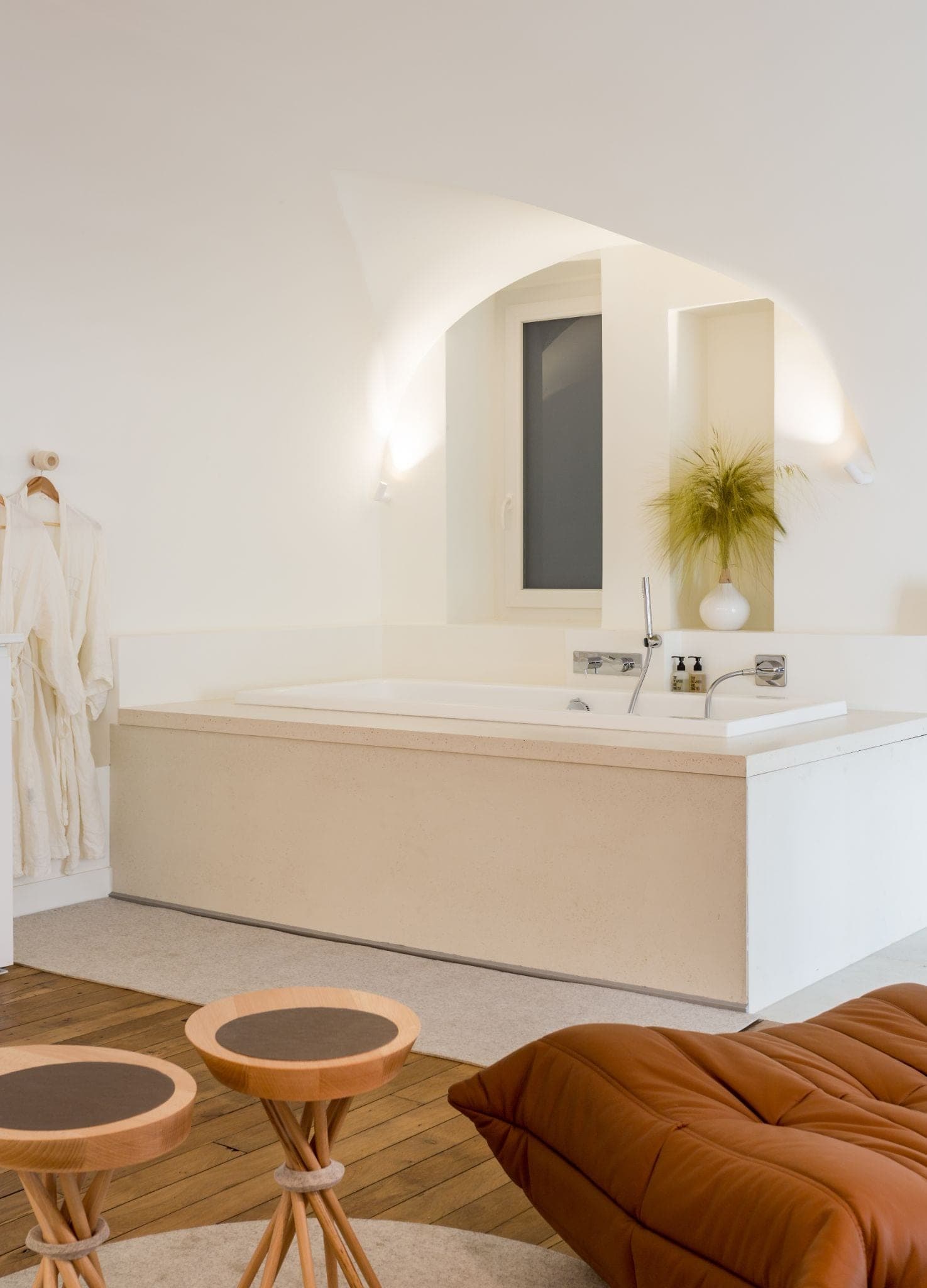 Baignoire sous une voûte, tabourets en bois et fauteuil en cuir cognac
