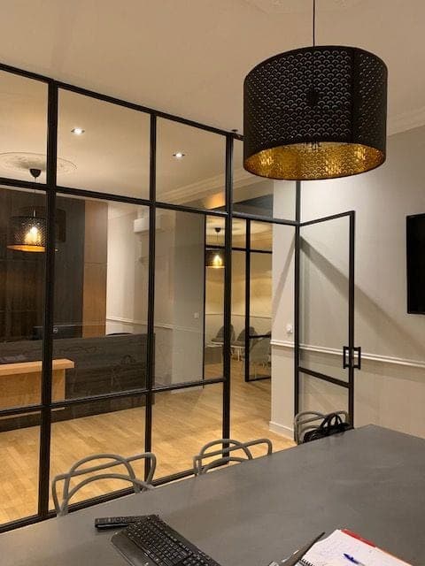 Verrière d’atelier noire avec porte vitrée, sous une grande suspension ajourée